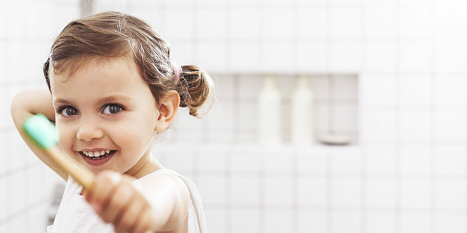 A little girl smiling brightly while holding a toothbrush in a bathroom