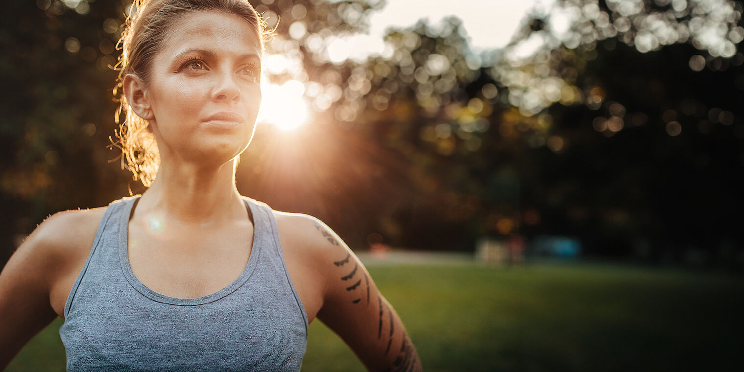 "Portrait of a confident young woman in workout gear standing outdoors with the sun setting behind her."